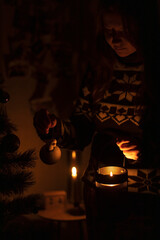 Ukraine, winter 2022. A woman decorates a Christmas tree in the dark with a candle.