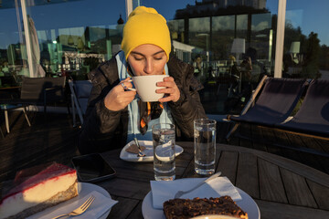 A girl in a yellow hat drinks in a cafe on the roof of the university, Austria, Salzburg
