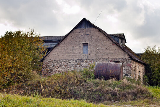 rural landscape, in the photo an old stone hayloft building and a wheat storage building against a gray sky with clouds