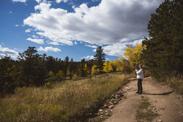 Obraz premium Woman walking in a field carrying a basket of flowers in the rocky mountains - dirt road, foraging, sustainable lifestyle