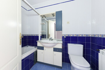 Toilet with blue and white tiles separated by a border and matching bathroom cabinet with integrated mirror