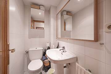 Small bathroom with mirror-door cabinet, light-wood framed mirror, and porcelain sink