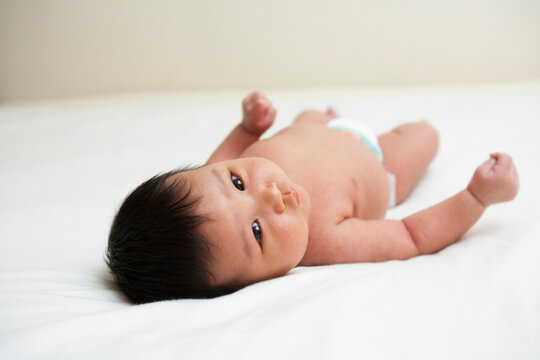 Newborn Asian baby in diaper, looking up at camera, studio shot on white background