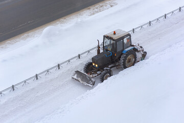 The tractor with the help of a bucket cleans the pavement from snow. Snowblower.