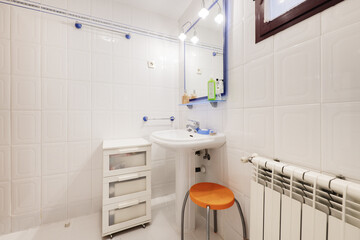 Bathroom with white wooden furniture with drawers, a porcelain sink with a matching foot and a mirror with blue glass shelves