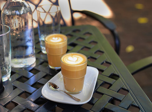 Two cortado coffees in glasses on outdoor, patio table with water bottle and glass, Canada