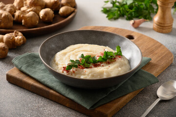 Jerusalem artichoke puree in plate decorated parsley on gray background. Close up.