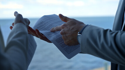 Man showing contract details at sea view. Hand holding pointing document closeup