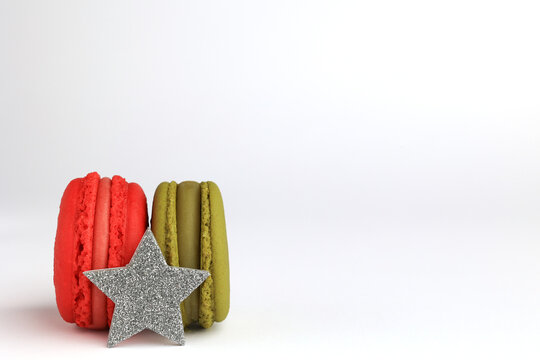 Two macaroons of red and green color, silver glitter star, light background, side view, place for text