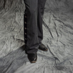 A man in elegant trousers with buttons, close-up. Portrait in the studio on a gray fabric background