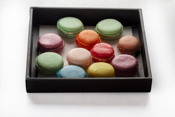 Assorted colorful macarons in elegant black gift box on white background overhead view French pastry dessert