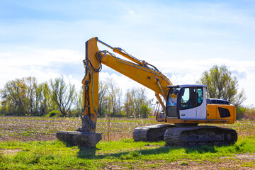 Yellow large excavator on the dike and forest in Germany.