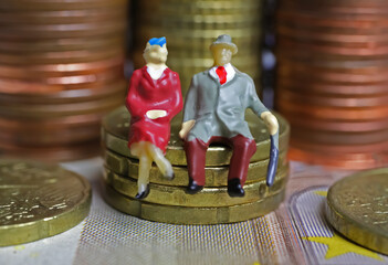 Abstract isolated figures of a retired old couple sitting on a stack of euro coins money - pension...