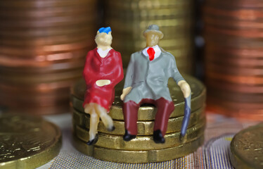 Abstract isolated mini figures of a retired old couple sitting on a stack of euro coins money - pension and retirement savings concept
