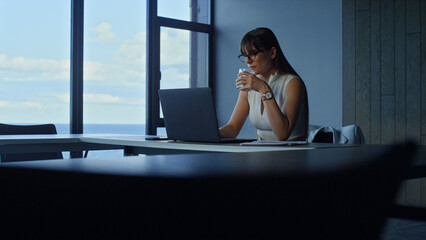 Employee holding water glass in office. Focused manager working laptop online