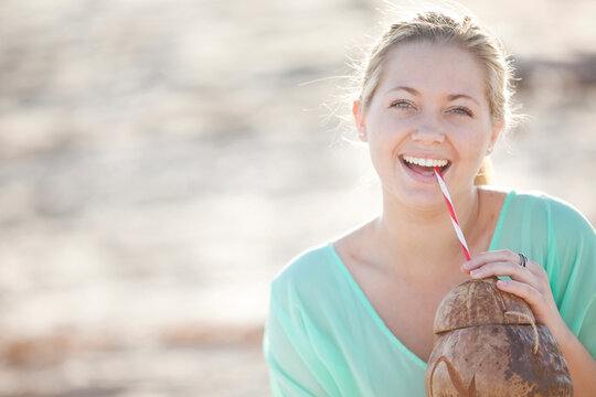 Close-up Portrait of Young Woman on Beach, Looking at Camera and Smiling, Drinking from a Straw out of a Coconut, Palm Beach Gardens, Palm Beach County, Florida, USA