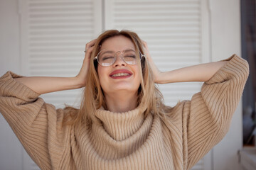 Stylish and beautiful young student with glasses and beige oversize sweater. Young woman wearing braces and smiling