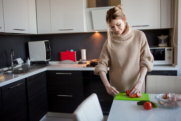 Lovely young woman at home in the kitchen, preparing a healthy meal. Beautiful charming blonde in her apartment