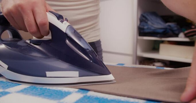 Man in undershirt and bare legs, ironing his trousers on an ironing board. Close up shot