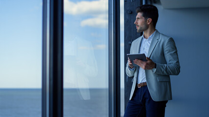 Happy businessman using tablet computer in ocean view office. Worker lifestyle