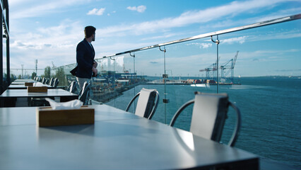 Pensive man resting alone on glass restaurant terrace. Freelancer looking sea