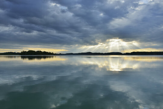 Clouds and crepuscular sunrays refelcted in lake at sunrise, Woerthsee Lake, Upper Bavaria, Fuenfseenland, Germany