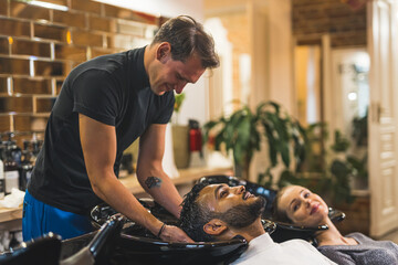 Positive hairstylist man washing his client's black hair. Modern hairdresser salon interior. Happy...