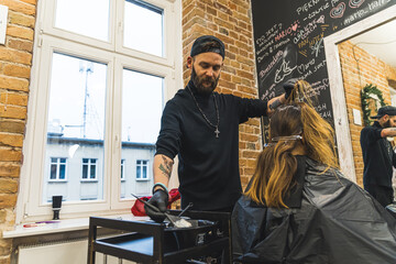 Hair bleaching concept. Professional male hair stylist adding bleach or hair dye with a brush to his client's hair. Low angle view. Hairdresser interior. High quality photo