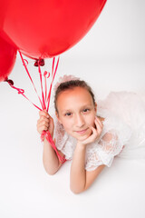 Fototapeta na wymiar Elegance girl of ten years old holding red balloons in hand and positive looking at camera. Studio high angle shot of Caucasian model lying down on white background. Part of photo series