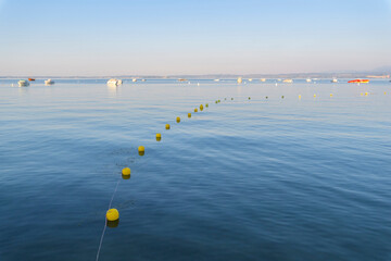Lake Garda (Lago di Garda) with line of buoys and boats anchored in the distance at Bardolino in Veneto, Italy