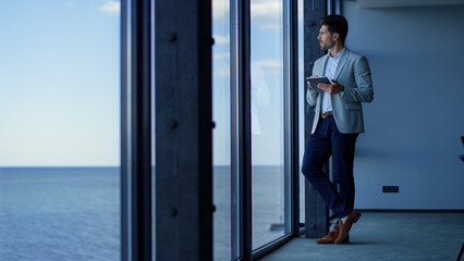 Focused entrepreneur using tablet in sea view office building. Business concept