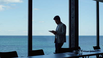 Thinking businessman using tablet in panoramic window office. Executive working