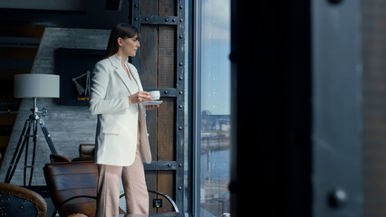 Fototapeta na wymiar Thinking woman drinking coffee at panorama window. Lady resting with beverage