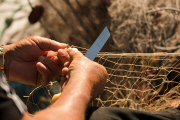 fishing net in the hands of fisherman, weaves and repairs by sewing the nets with a razor