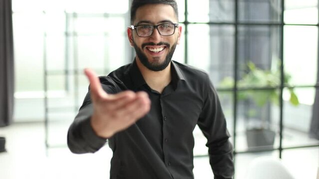 Young man with eyeglasses welcomes you with a handshake