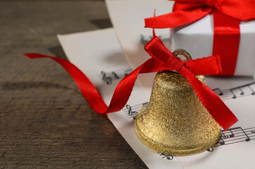 Bell, gift box and music sheets on wooden table, closeup with space for text. Christmas decor