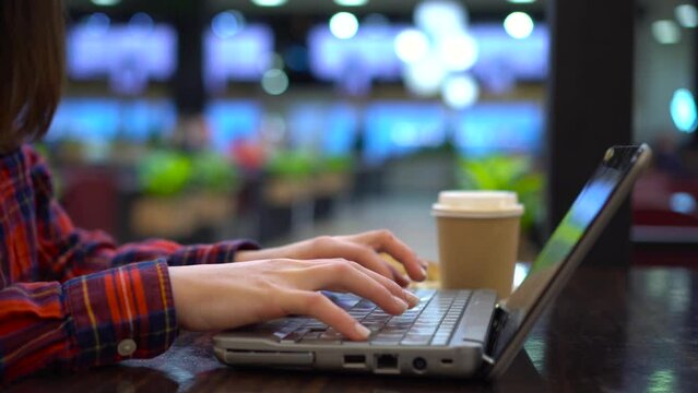 The girl is typing on a laptop while sitting in a cafe. Woman's hands close up.