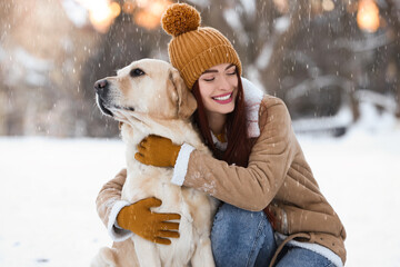 Beautiful young woman hugging cute Labrador Retriever on winter day outdoors