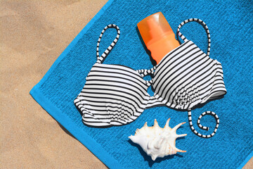 Blue beach towel, seashell, sunscreen and swimsuit on sand, top view
