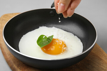 Woman salting fried egg at light grey table, closeup