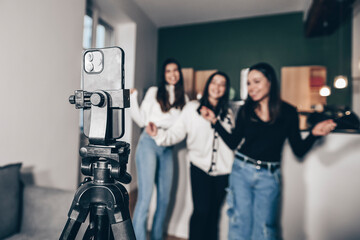 Close-up of a smartphone on a tripod filming 3 young white girls dancing, at home. Concept of making a living with videos on the Internet by being an influencer. Popularity and celebrity online