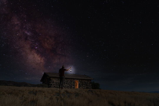 Man holding a lantern to view the Milky Way above a cabin
