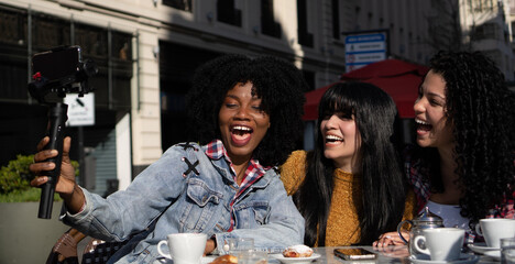 Young Latin friends laughing while video chatting at an outdoor coffee shop