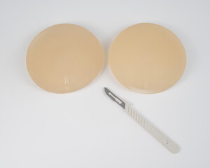 Breast silicone implants and a disposable scalpel on a white background. 