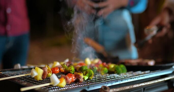 Footage of Friend group cooking meat on barbecue grill at new year party. Bar-B-Q or BBQ on traditional stove. Night Party, people and celebration concept.
