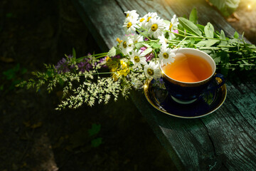 Herbal tea, cup of tea and bouquet chamomile flowers and wildflowers on wooden table in garden,...