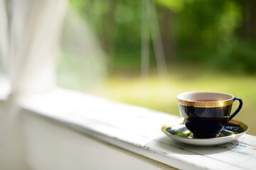 Closeup cup of tea in white wooden table outdoor, blurred green nature background