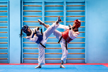 Portrait of two young women in kimono and suture, taekwondo athletes wrestling in the gym. Sportswomen demonstrating taekwondo martial art, hard training concept - obrazy, fototapety, plakaty