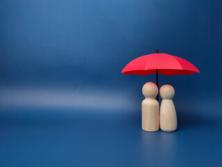 A couple of wooden dolls are hiding under a red umbrella, protecting wooden peg dolls, planning, saving families, preventing risks and crises, health care and insurance concepts.