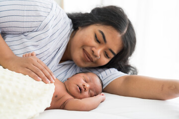 Smiling mother and newborn baby on bed. Young mom or nurse taking care newborn on bed in the hospital